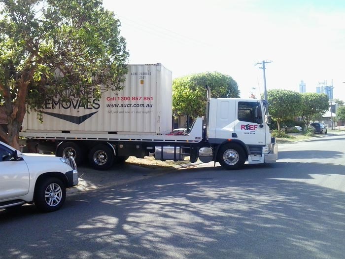 Tilt Tray Truck exiting driveway with large container