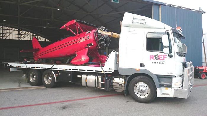 Reef Groups Slide Truck carrying a small airplane out of garage
